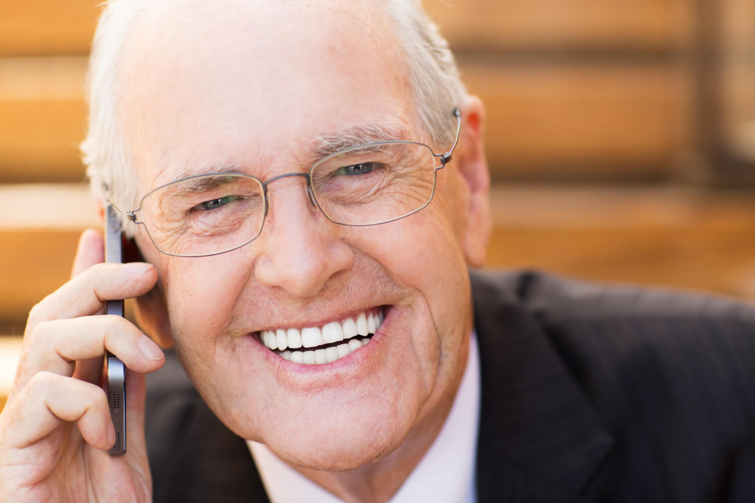 Homem idoso de terno e óculos sorri confiante enquanto fala ao celular, exibindo dentes saudáveis. Exemplo de reabilitação oral na Clínica Adachi em Santo André.