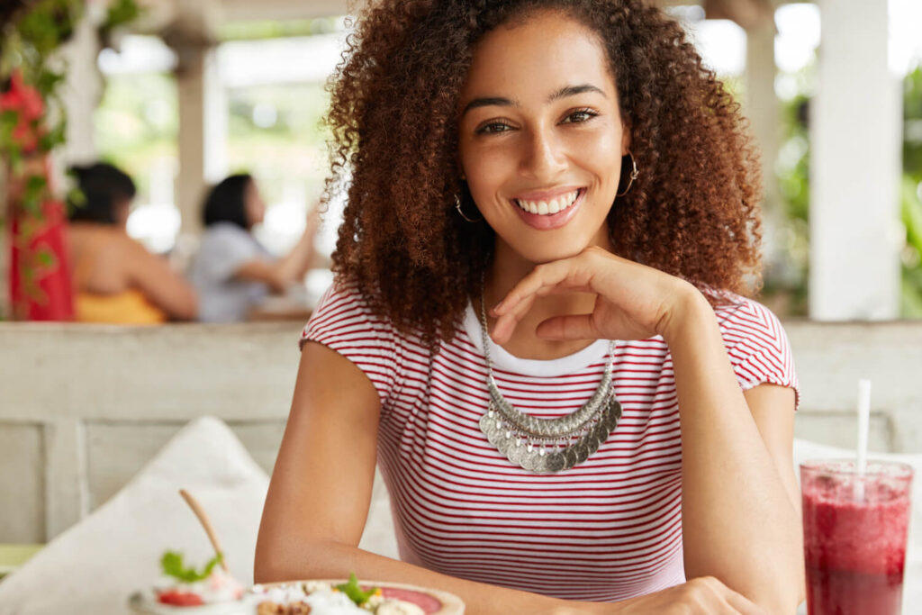 Mulher negra sorrindo em um restaurante, destacando a resistência das lentes de contato dental a manchas de alimentos em Santo André.