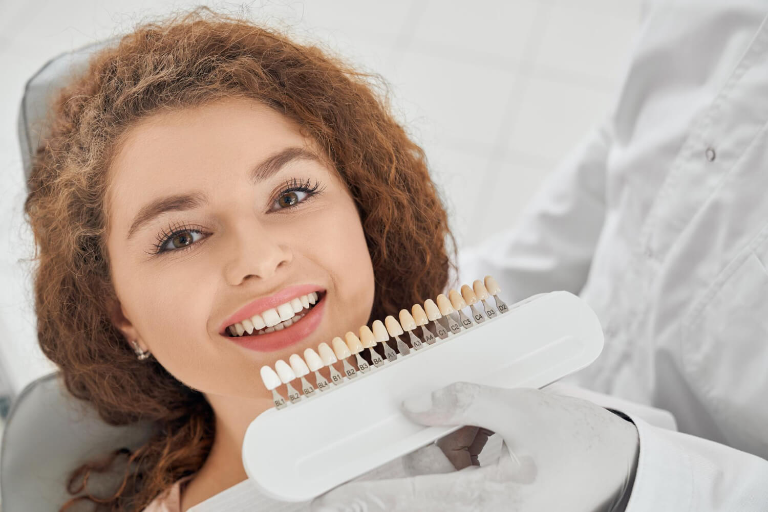 Paciente sorridente com facetas de resina enquanto dentista utiliza guia de cores na Adachi Odontologia em Santo André.