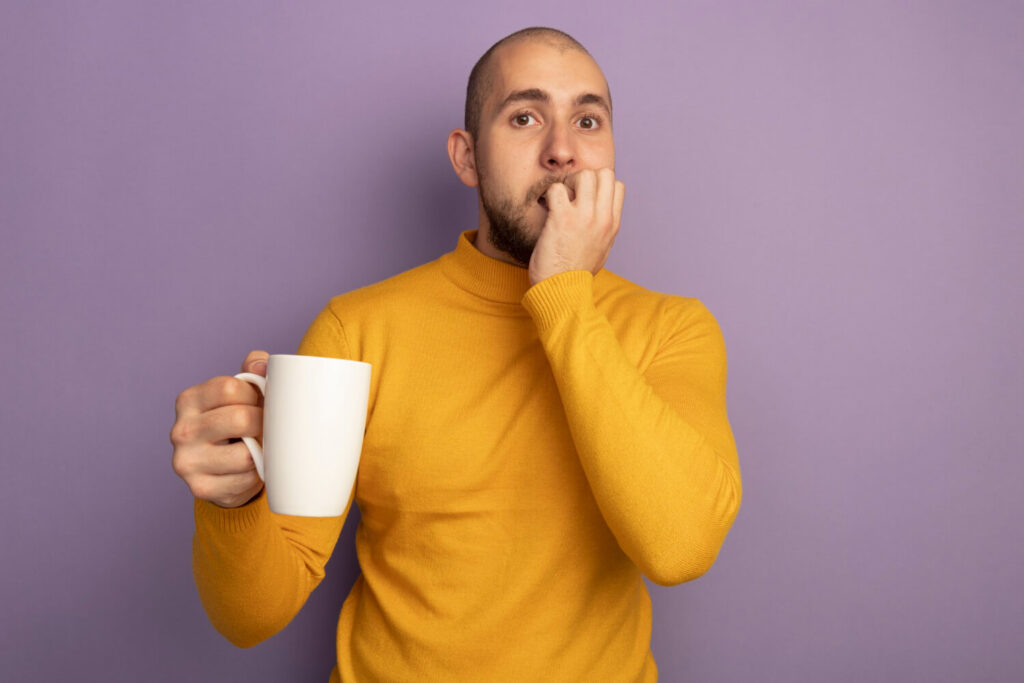 Homem expressa desconforto e sensibilidade nos dentes ao segurar caneca de café, buscando tratamento na Adachi Odontologia em Santo André.