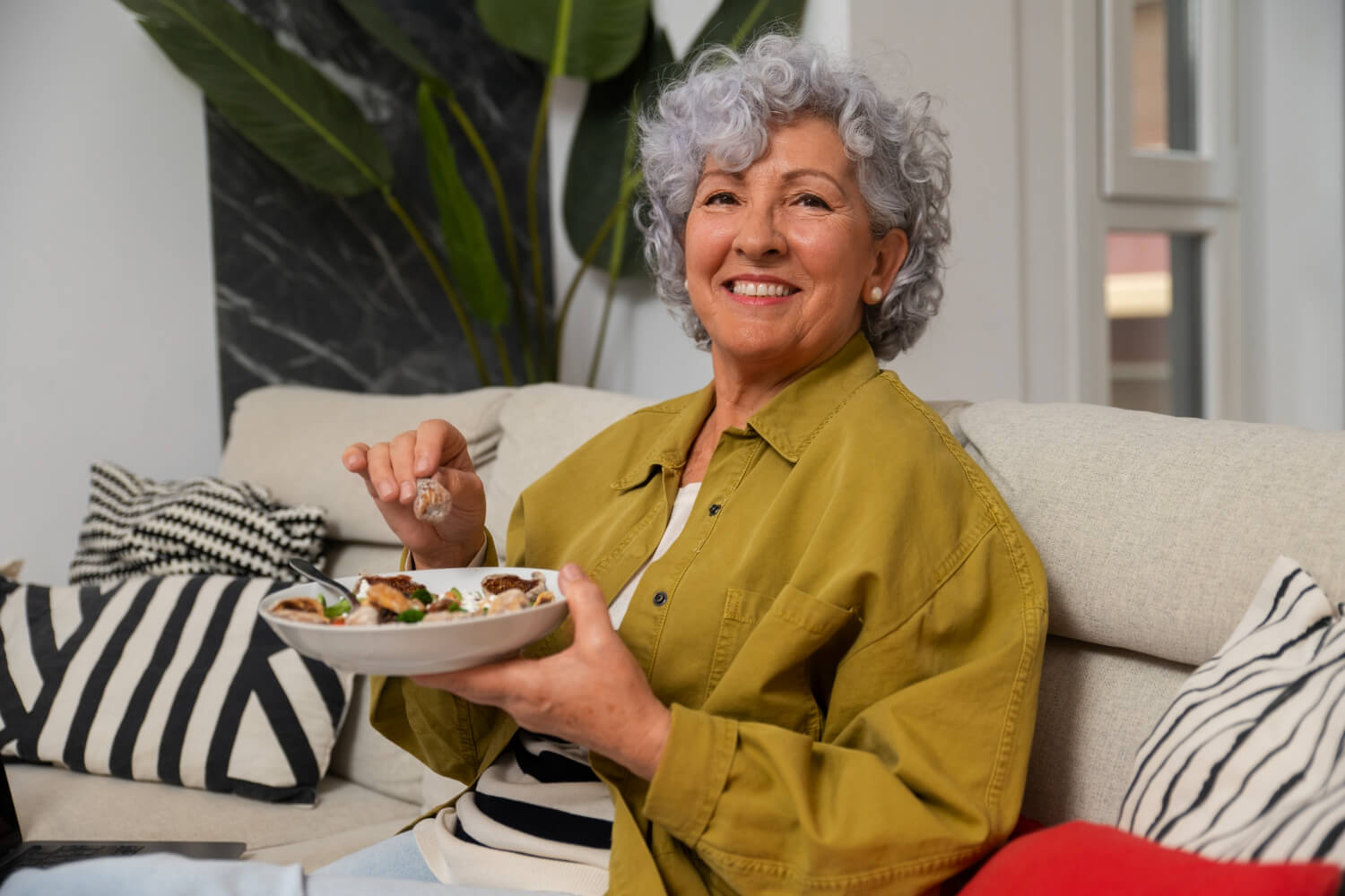 Mulher idosa sorridente segurando prato de comida, demonstrando segurança ao mastigar com prótese protocolo na Clínica Adachi em Santo André.